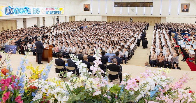 A large auditorium filled with people, with a floral display in the foreground