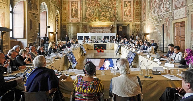 Personas sentadas alrededor de una mesa en una sala con cuadros históricos adornando las paredes.