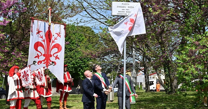 Tres personas descubriendo una placa y cuatro integrantes del cuerpo de cornetas con la bandera de Florencia.