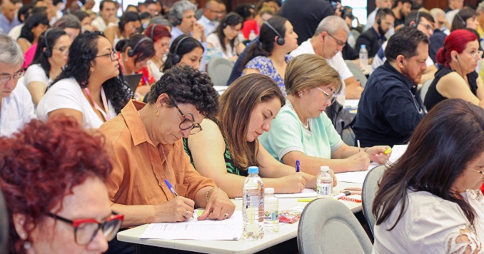 Personas sentadas en una sala tomando notas durante una conferencia.