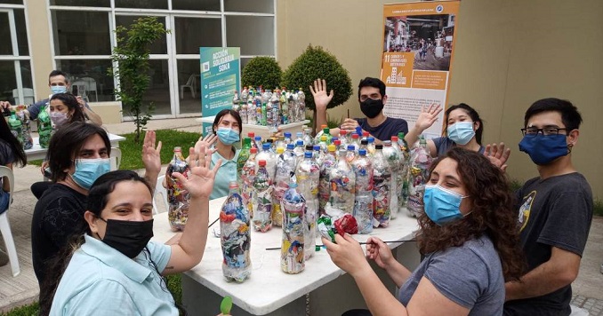Young people wearing masks sitting around a table that has plastic bottles on it