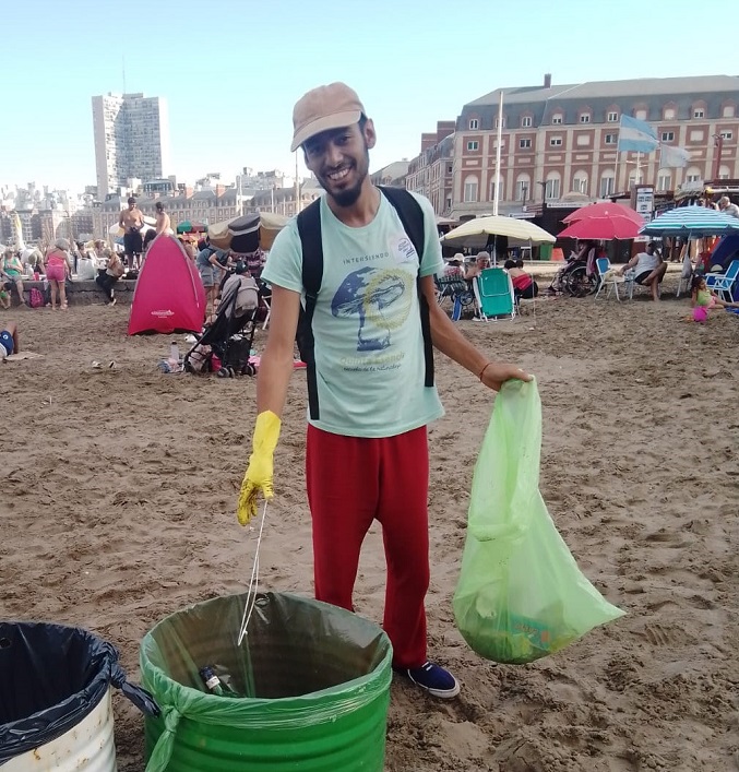 Young man in a hat and a T-shirt clearing garbage from the beach.