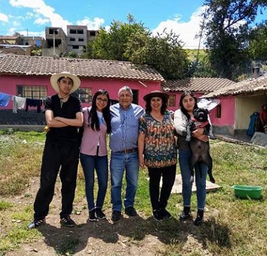 Five people posing for a family photo outside on a sunny day, the woman on the right is holding a black dog.
