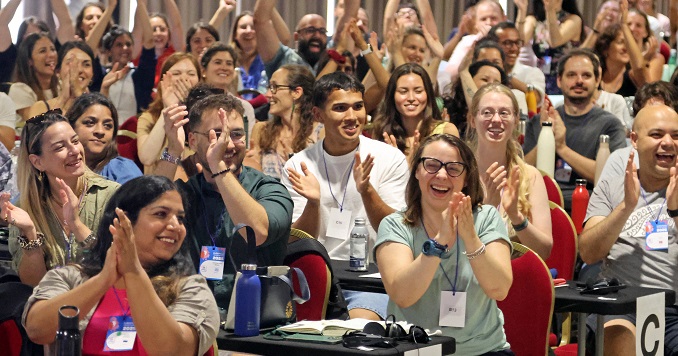 Lots of young people in a conference room, raising their arms and applauding. 