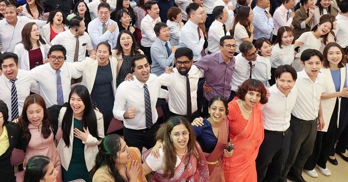 Young people singing together, standing  arm in arm in a large hall.