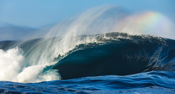Wave crashing into the deep blue ocean with a rainbow in the spray.