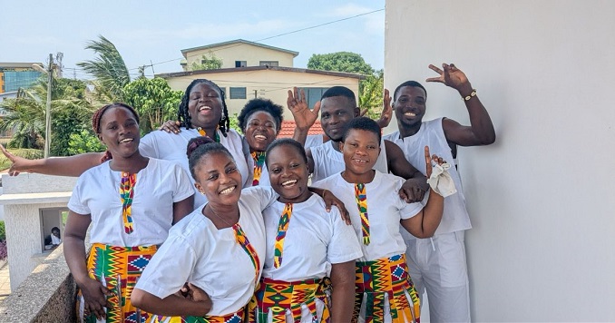 A group of young people with their arms around each other, laughing and smiling at the camera.
