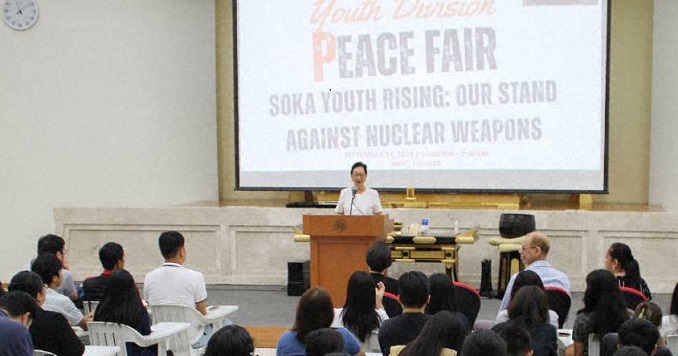 一位演讲者站在大型会议厅的讲台上向着观众发表演说。
