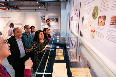 A group of people smiling while viewing an exhibition panel.