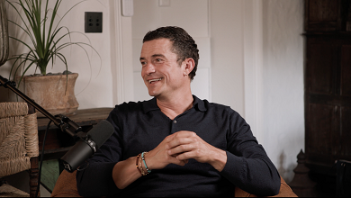 Orlando bloom smiling as he’s seated in front of a microphone.