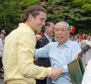 Daisaku Ikeda greeting Orlando Bloom outside as a smiling crowd looks on.