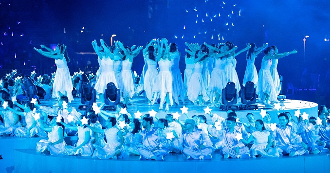 Dancers dressed in white onstage holding lights.