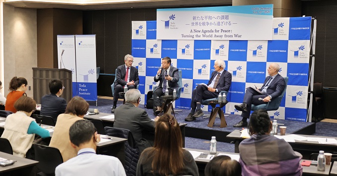 Four panelists on stage in front of an audience seated at tables.