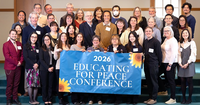 Group of people pose for a commemorative photo with a banner saying “Educating for Peace Conference”