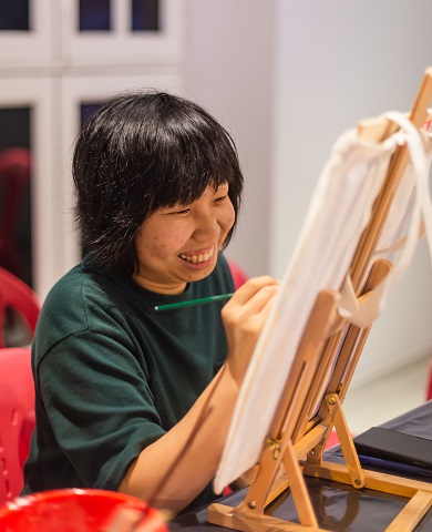A woman smiling while drawing at a small easel.