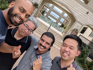 Group photo of Kiran (second right) and three men together outdoors smiling.