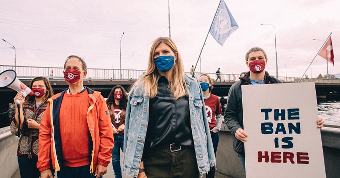 A group of people including Ms. Fihn stand at a waterfront with a sign reading “the ban is here”