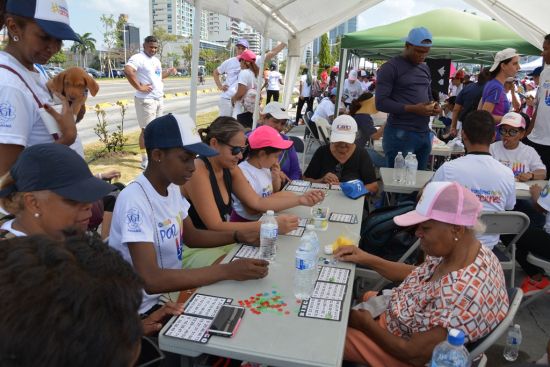 People of various ages sit at outdoor tables under canopies playing bingo and other games