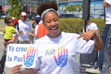 A young woman holds a sign in Spanish that reads “I create peace”