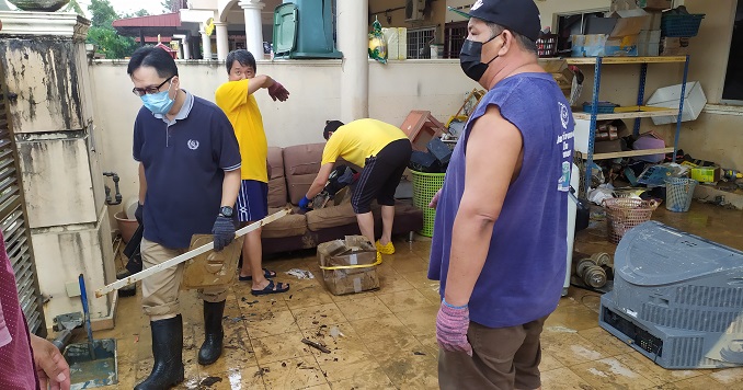 A group of exhausted-looking men amidst household items in a flood-damaged courtyard.